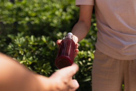Woman's hand giving a glass bottle of nutritious juice drink with plant leaf backgroundの写真素材