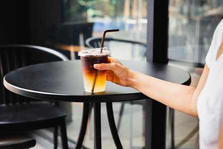 Woman drinking iced coffee in takeaway plastic cup at table outdoor cafeの写真素材