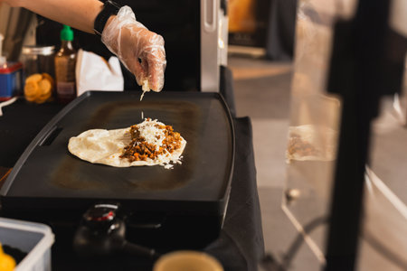 Chef sprinkles a tortilla with cheese preparing fresh quesadilla on black grill.の写真素材