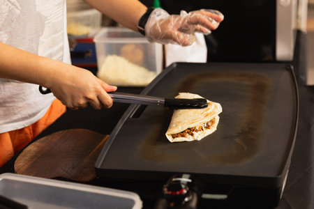 Woman preparing fresh quesadilla on black grill at local food marketの写真素材