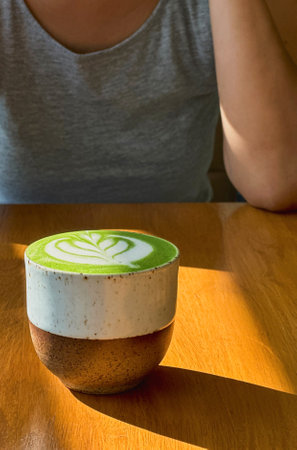 Cup of matcha latte green tea on wooden table with woman in backgroundの写真素材