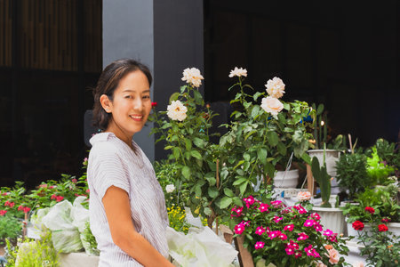 Beautiful woman working at flowers store holding blooming potted rosesの写真素材