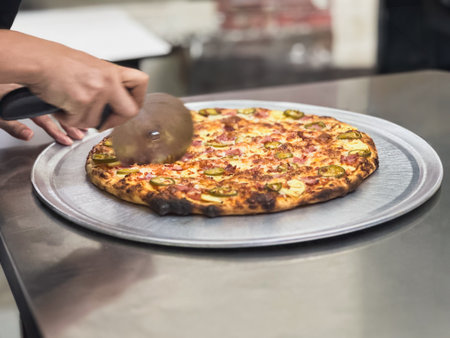 Woman chef using pizza cutter to cut slices of freshly baked pizza in pizza shopの写真素材