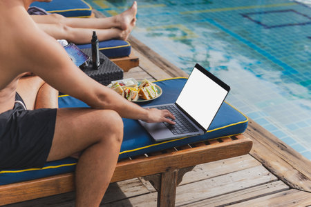 Man working on laptop on vacation eat club sandwich by the poolの写真素材