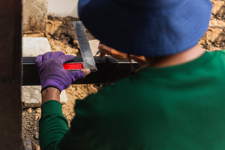 Male worker measuring iron with metal ruler in building siteの写真素材