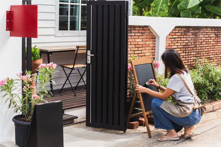 Woman owner writing menu on board outside cafe.の写真素材