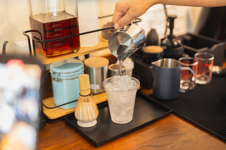 Barista hand pouring water from pitcher in to a glass with icedの写真素材