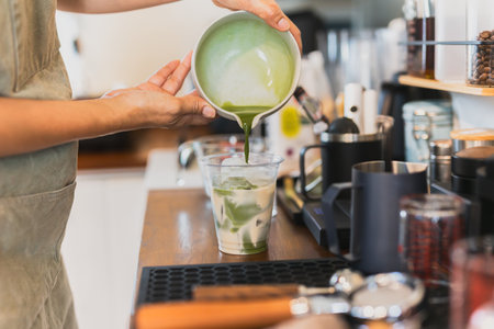 Woman barista pouring Matcha into glass with milkの写真素材