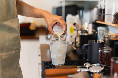 Woman barista preparing coffee latte pouring milk into a glass with icedの写真素材