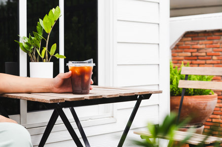 Person's hand holding iced coffee on table outside.
