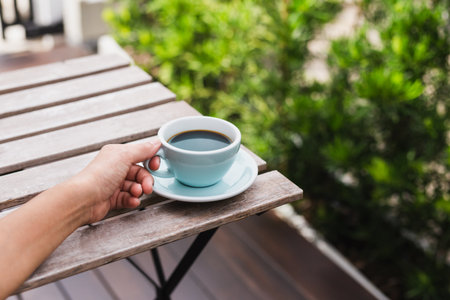 Female hands holding cups of coffee on wooden table outdoors.の写真素材