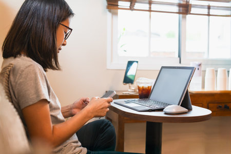 Woman hands using mobile phone while working with laptop in cafe.の写真素材
