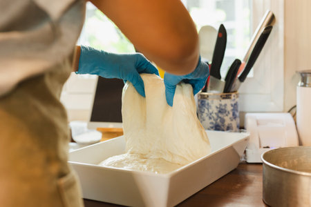Woman hand with glove preparing bread dough on wooden table.の写真素材