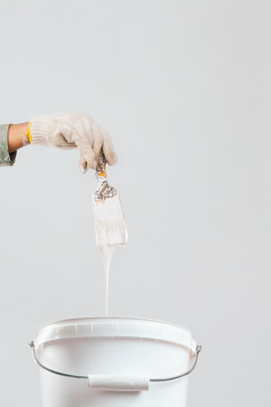 Painter holding a brush with white paint dripping into a bucket isolatedの写真素材