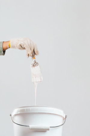 Painter holding a brush with white paint dripping into a bucket isolatedの写真素材