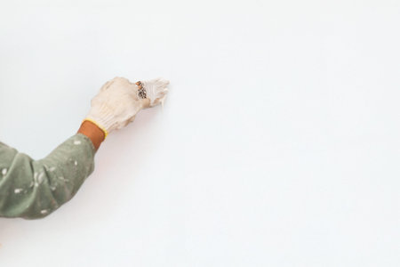 Gloved hand applying white paint to a smooth wall in white backgroundの写真素材