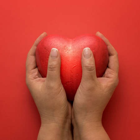 Female hands giving red heart on red background.の写真素材