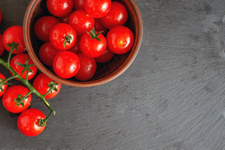 Fresh cherry tomatoes on branch on a black stone plate with copy space.の写真素材