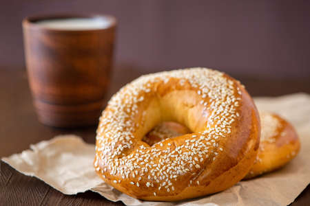 Two bagel with sesame and cup of milk on a dark wooden table. Side view, close up.の写真素材