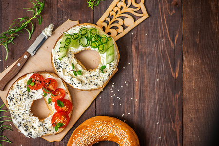 Bagels with cream cheese, sesame, tomato and cucumber on a wooden Board. Top view flat lay. With copy space.の写真素材