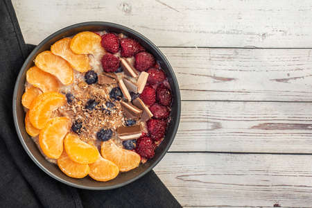 Oatmeal with tangerine, blueberries, chocolate and raspberry on light wooden table. Top view. With...