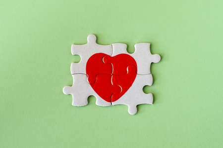 closeup of four pieces of a puzzle with red heart on green background background.