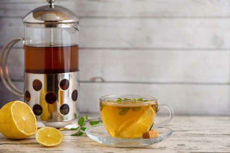 Cup of Lemon tea with cane sugar, french press and lemon slices on light wooden table.の写真素材