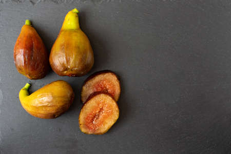 Whole figs and fig sliced on black stone plate. Top view.