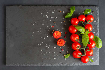 Fresh cherry tomatoes on branch with spices on a black stone plate. Copy space.の写真素材