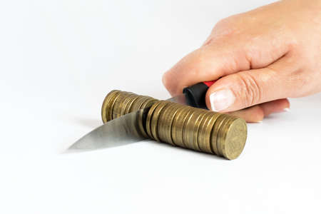 Knife cutting a pile of coin. Concept of budget cuts, savings, recession, commission, cash back, taxesの写真素材