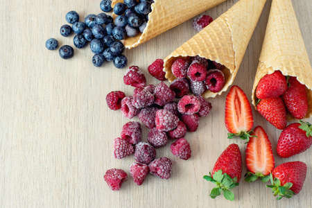 Strawberry, blueberry, raspberry in waffle cones on light wooden background.