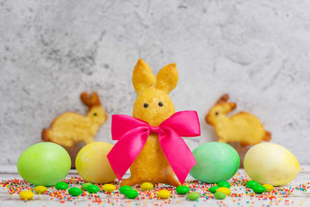 Homemade rabbit-shaped cookies with a red bow and Easter eggs on a light background.の写真素材
