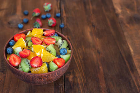 Healthy fresh fruit salad in bowl on dark wooden table. With copy space.の写真素材