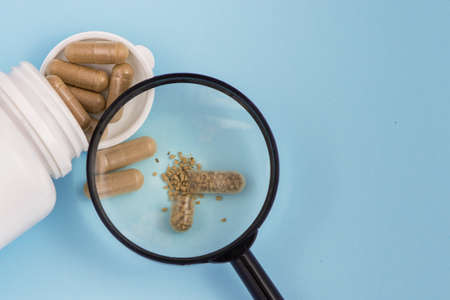 Organic pills in a medical jar seen from a magnifying glass on blue background. With copy space.の写真素材