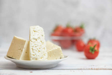 Large pieces of feta cheese in white plate and cherry tomatoes on light background. Selective focus, High key.の写真素材