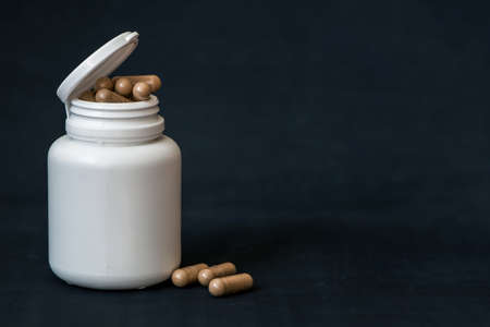 White pill bottle with organic capsules on a dark background. With copy space.の写真素材