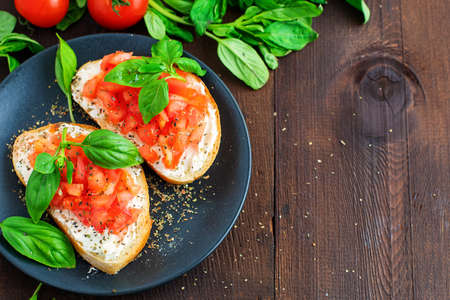 Traditional toasted Italian tomato bruschetta with spice and basil on dark wooden board. Top view vith copy space.の写真素材