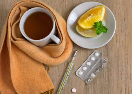 Concept illness, colds, cure. Cup of tea, thermometer, pills and a knitted scarf. On light backgroundの写真素材