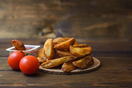 Grilled potatoes with cherry tomatoes and sauce on a cork stand on a dark wooden background.