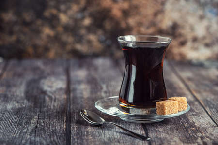 Turkish glass for tea bardak with cane sugar on dark wooden table.の写真素材