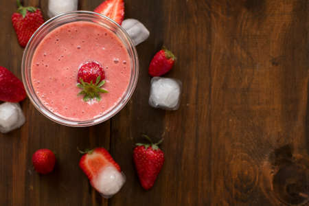 Strawberry Banana Smoothies in Glasses with ice cubes and Ingredients on dark wooden Table.の写真素材