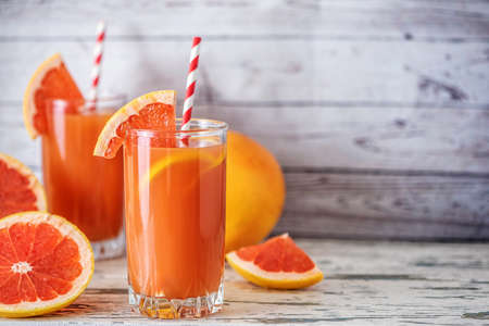 Fresh grapefruits and two glasses of grapefruit juice on light wooden table. With copy space.の写真素材
