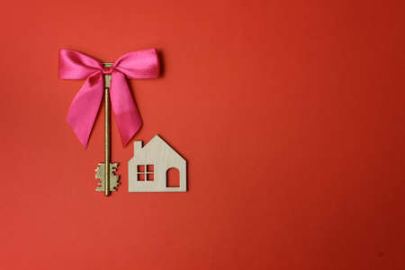 Gift with pink ribbon and a vintage key near layout of the house on the red background.の写真素材