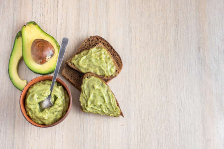 Fresh avocado cream in wooden bowl with bread slices on light background. Top view. With copy space.の写真素材