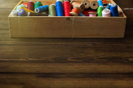 Colorful threads in box on wooden background with copy space.