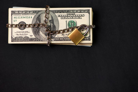 Safe secure chain locked stack of hundred dollar bills on dark background with copy space.の写真素材