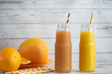Fresh grapefruits, orange and two glasses of grapefruit and orange juice on light wooden table.