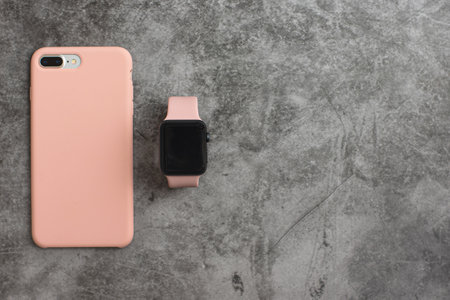 KROPIVNICKY, UKRAINE - MAY 13, 2019: The black Apple Watch with pink bracelet next to the iPhone in a pink case on a gray background. With copy space. Top view.の写真素材
