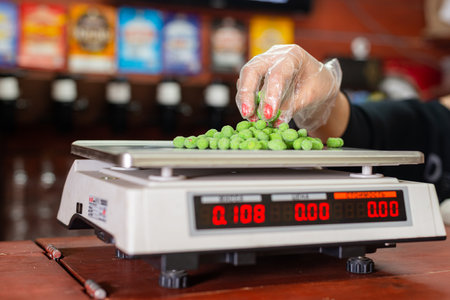 On an electronic scale, the seller weighs salted nuts, in the background is a beer showcase.の写真素材