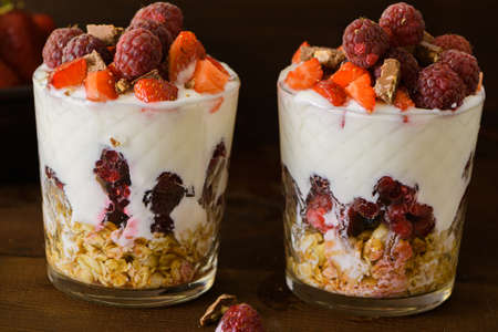Natural Greek yogurt with fresh berries and muesli in a glass. Healthy food, healthy lifestyle, the concept of the menu of sports fitness nutrition. On a brown background.の写真素材